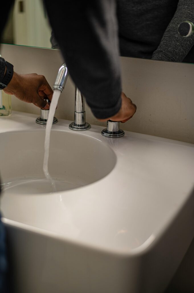 pexels-photo-7327156-7327156 Close-up of hands adjusting water flow in a modern ceramic sink with stainless faucet.