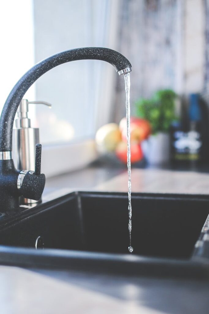 water-kitchen-black-design-6256 A modern kitchen sink with running water, a sleek faucet, and a vase on the countertop.